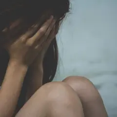 Kobieta ukrywa twarz w dłoniach, przygnębiona. Może to symbolizować trudności związane z wypowiedzeniem umowy o pracę a zwolnieniem lekarskim od psychiatry.