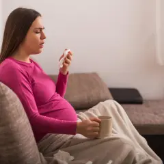 Ciężarna kobieta z kubkiem w dłoni i chusteczką, szukająca informacji co na kaszel w ciąży.
