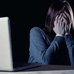 Kobieta z dłońmi na twarzy przed laptopem, zastanawia się, czy choroby psychiczne są dziedziczne.