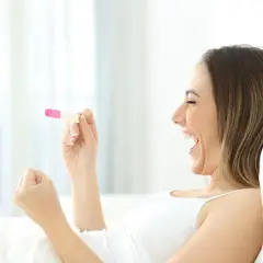 Kobieta z radością trzyma test ciążowy. To dowód, że jej marzenie o tym, jak zajść w ciążę, właśnie się spełnia!