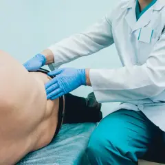 Lekarz w rękawiczkach bada pacjenta, pokazując, jak wygląda badanie urologiczne u mężczyzn.