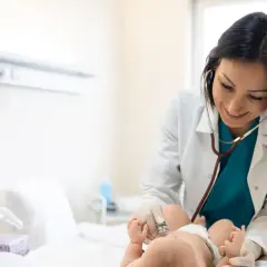 Uśmiechnięty neonatolog bada noworodka stetoskopem.