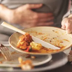 Osoba z ręką na brzuchu, symbolizująca jadłowstręt, trzyma brudny talerz po posiłku.