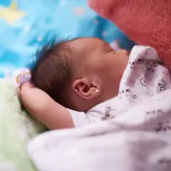 Słodkie niemowlę śpi otulone kocykiem w kotki, z małą perłową kolczykiem w uchu.