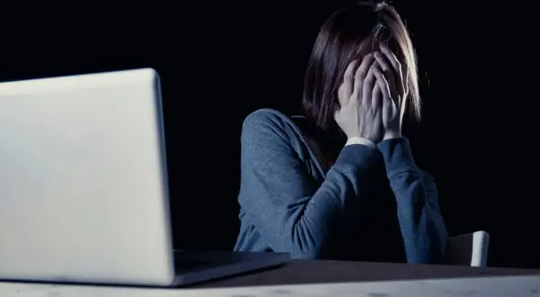 Kobieta z dłońmi na twarzy przed laptopem, zastanawia się, czy choroby psychiczne są dziedziczne.
