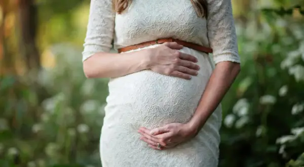 Kobieta w białej sukience delikatnie obejmuje ciążowy brzuch. Czy po owulacji można zajść w ciążę? To pytanie nurtuje wiele par.