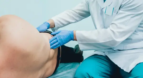 Lekarz w rękawiczkach bada pacjenta, pokazując, jak wygląda badanie urologiczne u mężczyzn.