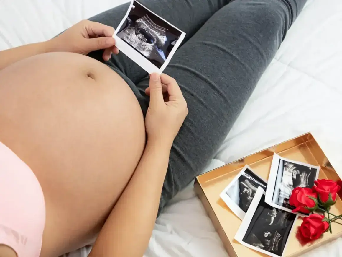 Kiedy widać brzuch w ciąży, przyszła mama trzyma zdjęcie USG. Obok leży pudełko z kolejnymi zdjęciami i czerwonymi różami.