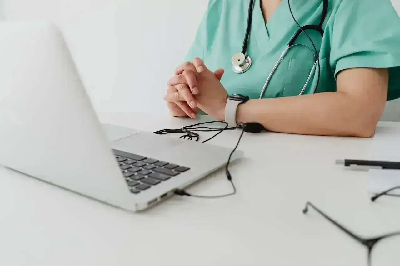 Lekarz w zielonym fartuchu z nasłuchiwaczem przy laptopie, gotowy do wystawienia psychiatra online e-recepty.