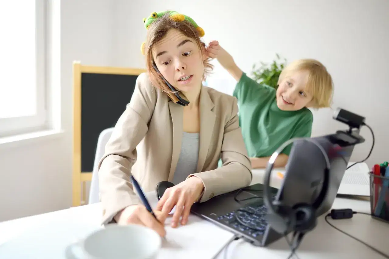 Pracująca mama z zabawką na głowie, rozmawiająca przez telefon, podczas gdy syn ją rozprasza. Czy ADHD jest dziedziczne?