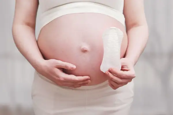 Ciężarna kobieta trzyma podpaskę, zastanawiając się, czy można mieć okres i być w ciąży.